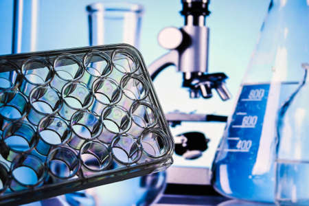 Achievements of modern biological science. A 24-well cell culture plate against an abstract...