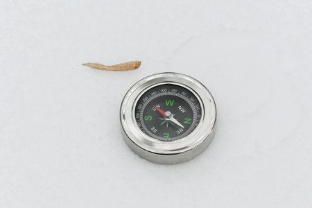 A compass in the snow. The compass is placed on the snow on a cloudy winter day.