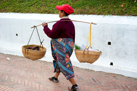 LUANG PRABANG, LAOS - 8 DEC, 2013: Unidentified woman sells goods by using traditional baskets on the streets of Luang Prabang - popular travel destination in Laos.のeditorial素材