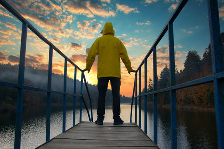 Man standing on the bridge over the lake in a yellow raincoat. View of Bozcaarmut at sunset.の写真素材
