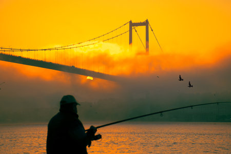 A fisherman fishing with his fishing rod in the foggy Bosphorus. The Bosphorus and the July 15 Martyrs' Bridge in the fogの写真素材