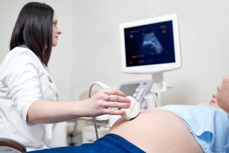 Female doctor using ultrasound and screening pregnant woman.