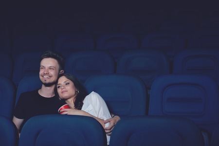 Smiling couple embracing and watching funny movie in cinema.