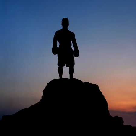 Dark silhouette of a muscular male boxer outdoors on sunsetの写真素材