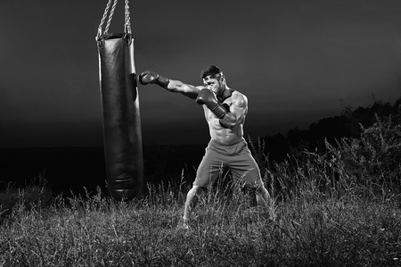 Monochrome shots of a male boxer training with a punching bag ouの写真素材
