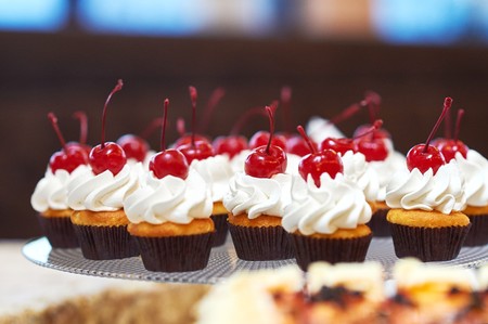 Plate full of cupcakes with cream and cherry on topの写真素材