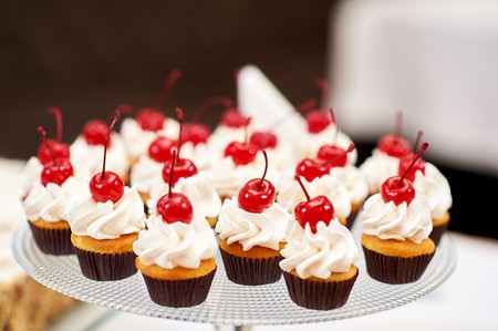 Plate full of cupcakes with cream and cherry on topの写真素材