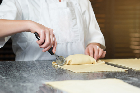 Baker makes some rolls from raw dough and filling, using special knife for doughの写真素材