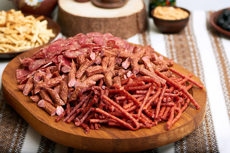 Close-up of bid wooden board served with great ammount of smoked thin sausages. Delicious snack for light alcohol like beer. It stands on the embroidered in ukrainian style tablecloth.の写真素材