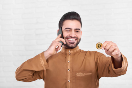 Smiling Arabian businessman keeps golden bitcoin.の写真素材