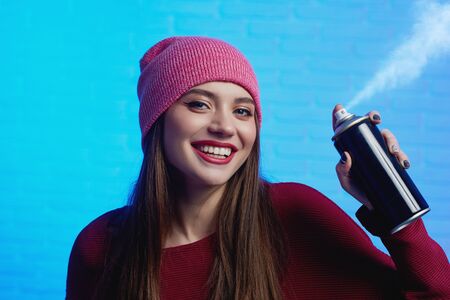 Smiling pretty female wearing red hat and sweater posing with paint sprayの写真素材