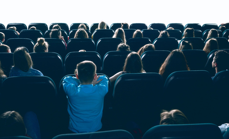 great ammount of people watching movie in big cinema hall, sitting on comfortable places. Backview of women, men and children entertaining in cinema house.の写真素材