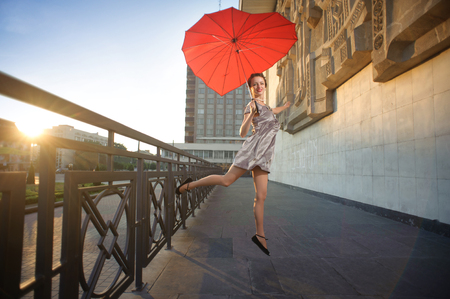 Ivano-Frankivsk, Ukraine - 1 June 2015 : young pretty dancing girl is jumping, holding heart-shaped red umbrella. There is interesting textured city buildings facade on background.のeditorial素材