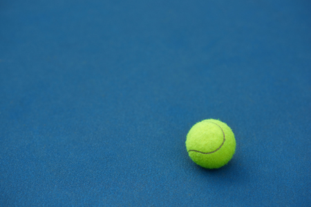Yellow bright tennis ball is lying on on blue carpet. Made for playing tennis. Contrast image with satureted colors. Blue tennis court.の写真素材