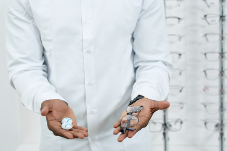 Man in white shirt is keeping optical eyeglasses standing in front of transparent stand with different lenses in fashionable, stylish, modern frames. Ophthalmological shop.の写真素材