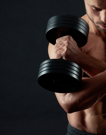 Cropped photo of athlete with strong muscular body keeping heavy metallic dumbbells with his hands crossed. Looking down, training hard. Having clear ABS relief, fit, athletic, sporty body.の写真素材