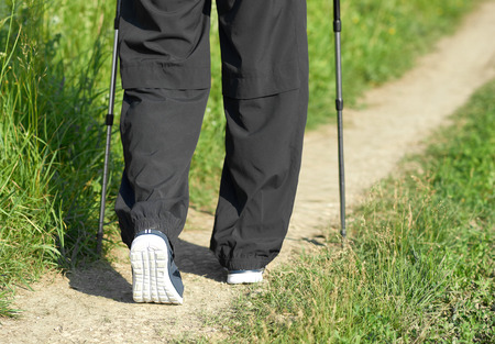 Man walking on sandy path wearing sneakers, using tracking sticks. Wearing black trousers. Cardioexercises outdoors on fresh air. Sport lifestyle. Sunny day. Healthy lifestyle. Keeping fit.の写真素材