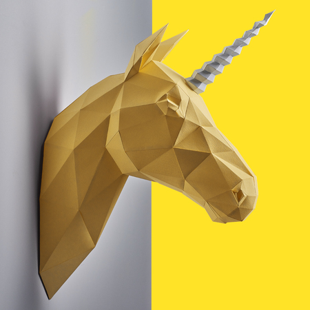 Fancy saturated yellow unicorns head made of paper hanging on grey wall. Innovative interior design details. Straight lines. Original geometrical shape.Shadows.の写真素材