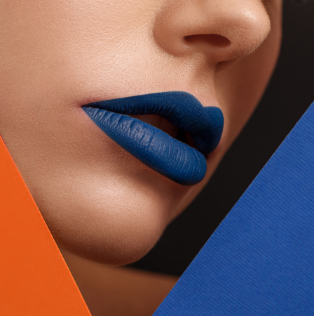 Close up of womans face with lips covered with dark blue lipstick. Models face surrounded by colorful yellow and blue carton sheets. Looking original, contrast. Posing on black studio background.の写真素材