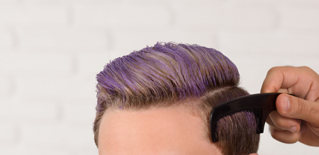 Young client with toned violet hair by professional barber. Hairdressers hands doing a hairdstyle...