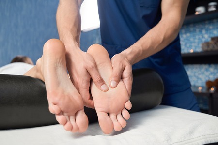 Closeup of hands of qualified masseur massaging foot of  female client in spa cosmetology salon. Woman lying on couch, relaxing and enjoying during healthy procedure. Concept of body care.の写真素材