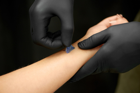Close up of hands in black gloves of master doing pattern of tattoo on clients skin. Crop of...