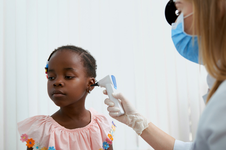 Portrait of adorable little girl in pink dress sitting in doctors office. Cute girl waiting looking away while professional nurse working and treating her. Concept of health care.の写真素材
