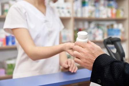 Unrecognizable pharmacist and customer in drugstore. Hand of man taking medicament, client buying in pharmacy. Chemist giving white pill bottle for health care, from disease.の写真素材