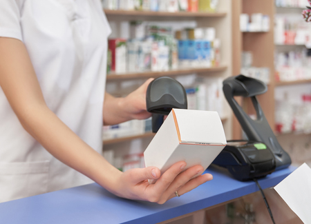 Cropped close up of pharmacist holding white medical box with medicines. Professional specialist scanning price using barcode scanner. Chemist working in drugstore.の写真素材