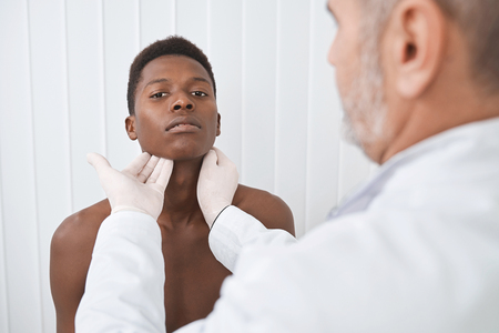 Medical specialist palpating lymph nodes, examining neck of patient. Young, handsome african man on...