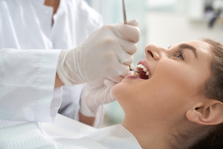 Closeup of woman lying on dental chair with open mouth and dentist in white protective gloves examining teeth. Female patient treating and caring about teeth. Concept stomatology and health.の写真素材