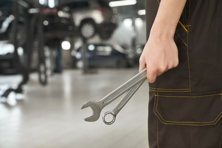 Close up of mechanic hand holding wrenches, special tools for repairment and fixing of vehicles. Man in overalls standing in autoservice.の写真素材