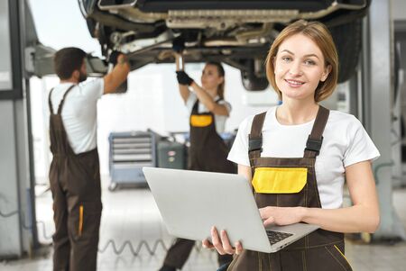 Front view of attractive woman working at auto service. Professional engineer in coverall keeping...