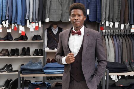 Handsome client of shop dressing grey suit, black waistcoat, white shirt and red bow tie posing, looking and camera. Huge choice of stylish, elegant clothing and footwear in fashion boutique.の写真素材