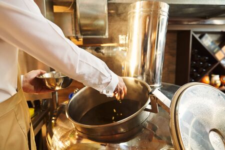 Close up of male hand of brewer adding hops in beer wort in metallic brew kettle. Modern technology of brewing beer.の写真素材