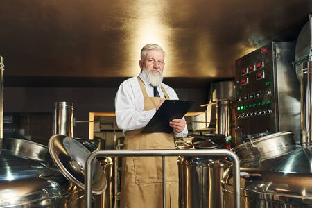 Professional brewery worker monitoring process of brewing beer. Handsome, elderly, bearded worker...