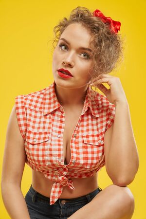 Portrait of seductive, beautiful model with sexy red lips and attractive decollete. Stylish, charming girl in checked shirt posing on yellow background. Sensual lady in style of pin up.の写真素材