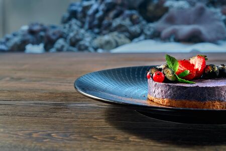 Side view of half of plate with delicious cake served with blueberry, red strawberry and fresh mint. Yummy dessert staying in restaurant. Piece of cheesecake on blurred background. Concept of food.の写真素材