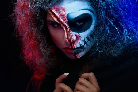 Close up of charming young lady with scared halloween makeup wearing black cape looking at camera...