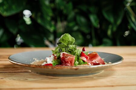 Delicious salad served on blue plate in restaurant. Dish made of strawberries, green salad, white sauce and prosciutto.の写真素材