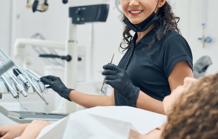 Cropped view of cheerful female dentist in uniform and protective gloves working with professional...