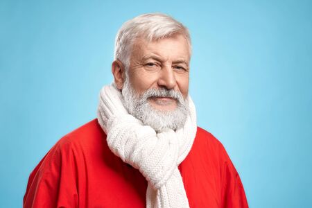 Portrait of confident senior man with real beard and grey hair wearing Santa Claus costume and white...