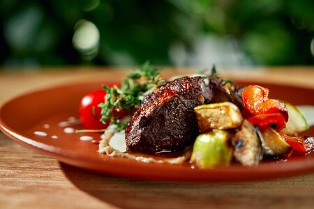 Main dish in restaurant. Grilled vegetables with duck steak and sauce served on plate.の写真素材