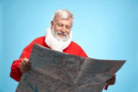 Mature bearded man with grey hairstyle wearing Santa costume and knitted scarf standing in studio...