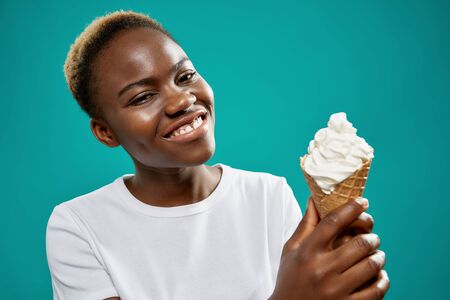 Front view of cute young woman keeping tasty ice cream and looking at camera and smiling on blue...