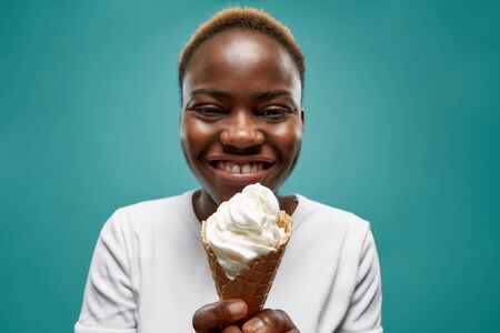 Selective focus of cheerful african woman eating tasty ice cream in summer. Young female keeping...