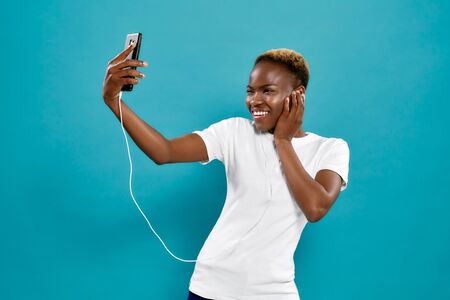 Front view of happy young female wearing white shirt taking self, laughing and posing in studio. Concept of fun and happiness.の写真素材
