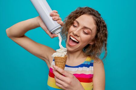Close up of happy, glamour girl holding wafer cone and applying whipped cream, smiling. Positive,...