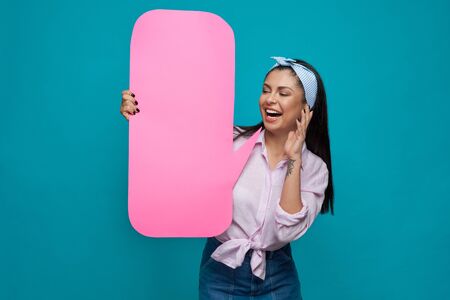 Beautiful, playful girl posing with pink paper speech bubble, smiling. Happy, positive model wearing...