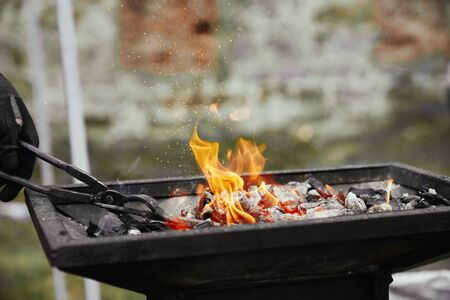 Close up of incognito blacksmith manually heating metal piece in burning fire. Man in gloves holding...